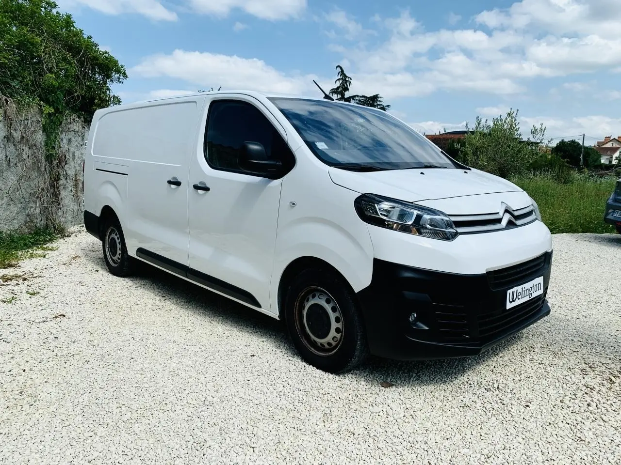 Fourgon Citroën Jumpy XL blanc vu en 3/4 avant droit, avec calandre noire et jantes acier sur sol gravillonné.