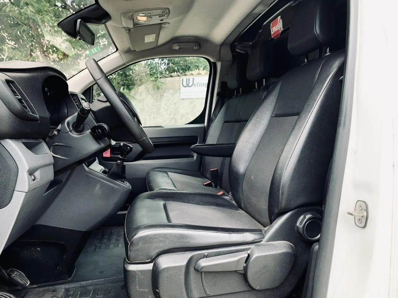 Vue intérieure côté conducteur du Citroën Jumpy blanc 2020, sièges noirs en cuir avec accoudoir et tableau de bord visible.