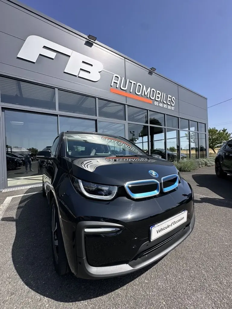 BMW i3 noire vue de face en léger 3/4 avant droit, avec calandre bleue distinctive et plaque "Véhicule d'Occasion" visible.