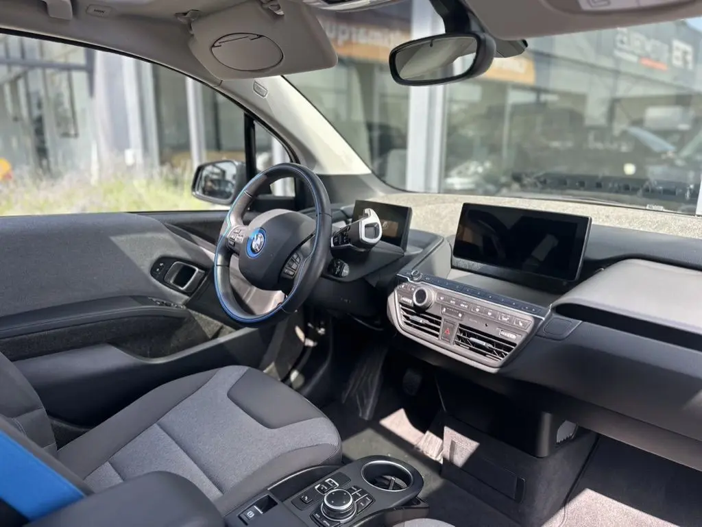 Intérieur de la BMW i3 noire 2022 vu côté conducteur, tableau de bord moderne avec écran tactile et volant multifonction.