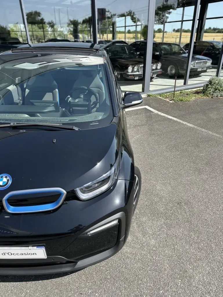 Vue 3/4 avant droite d'une BMW i3 noire électrique 2022 avec calandre bleue distinctive, stationnée devant une vitrine.