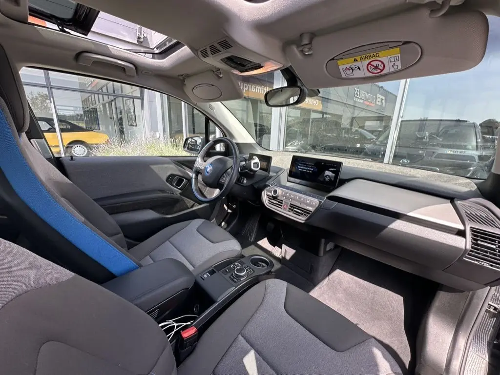 Vue intérieure côté conducteur de la BMW i3 noire 2022, mettant en valeur le tableau de bord moderne et les sièges gris avec appui-tête bleu.