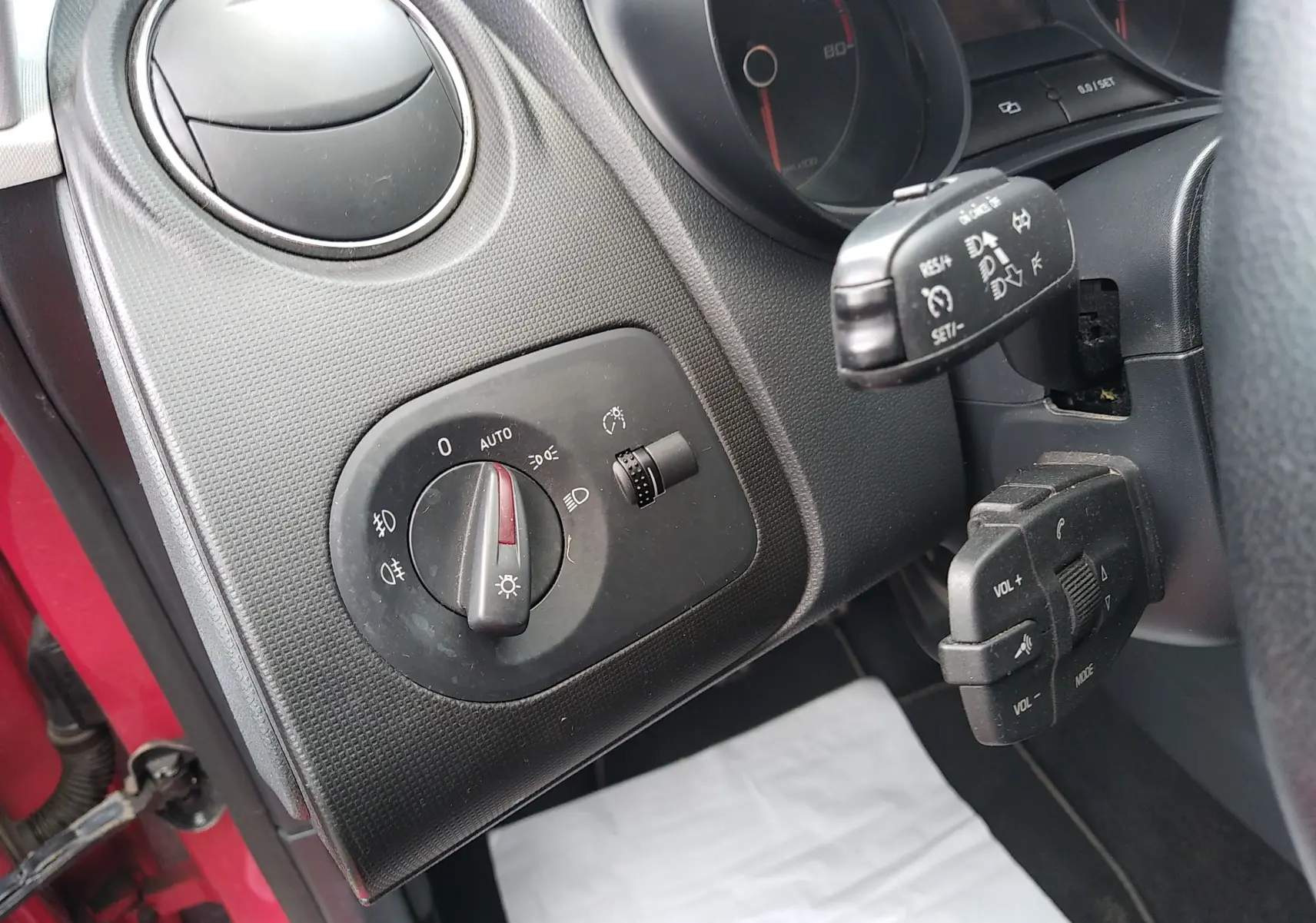 Détail du tableau de bord côté gauche d'une SEAT Ibiza ST rouge, avec commandes d'éclairage et régulateur de vitesse.