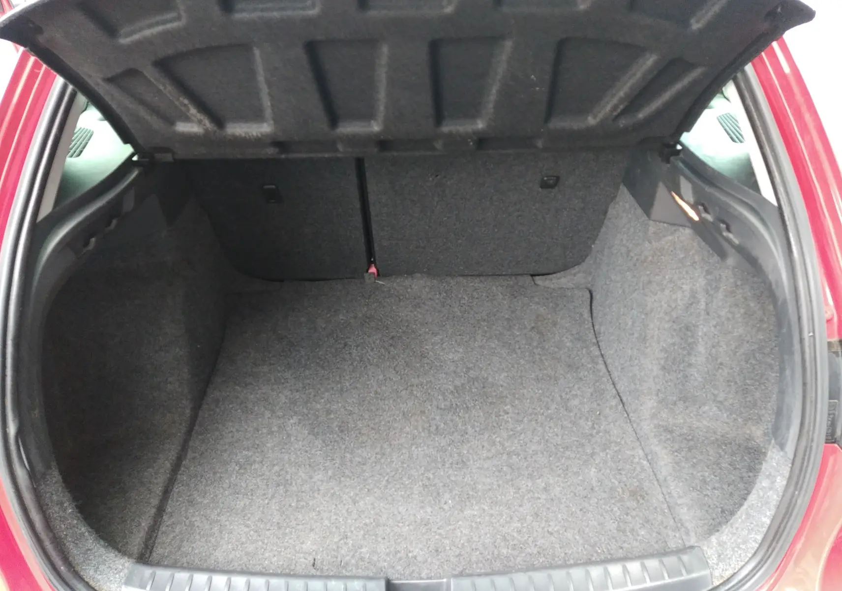 Coffre ouvert vu de l'arrière d'une SEAT Ibiza ST rouge de 2015, montrant un espace de chargement vide et propre.