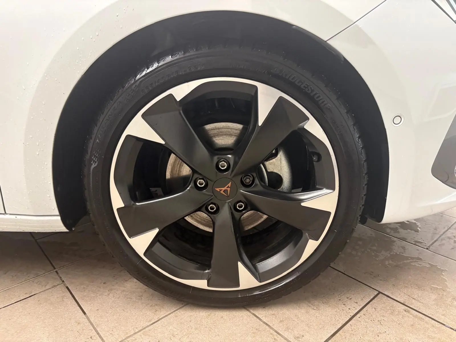 Gros plan sur la roue avant gauche de la CUPRA Leon blanche Nevada avec jante noire et argentée au design moderne.