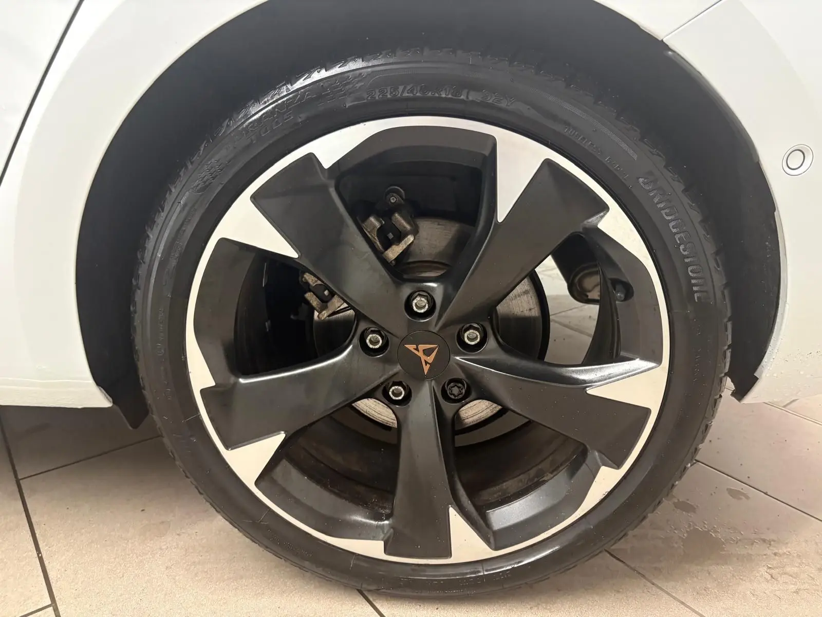 Gros plan sur la jante noire et argentée du côté avant droit d'une CUPRA Leon blanc Nevada, avec logo central distinctif.