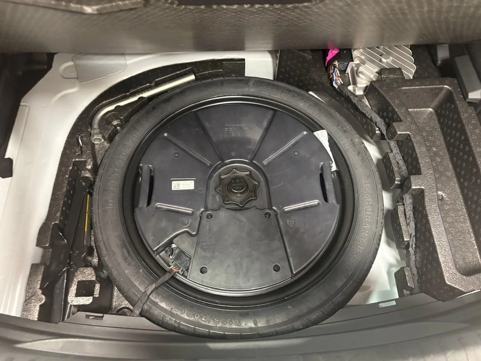 Vue rapprochée du pneu de secours noir dans le coffre d'une CUPRA Leon blanc Nevada 2024.