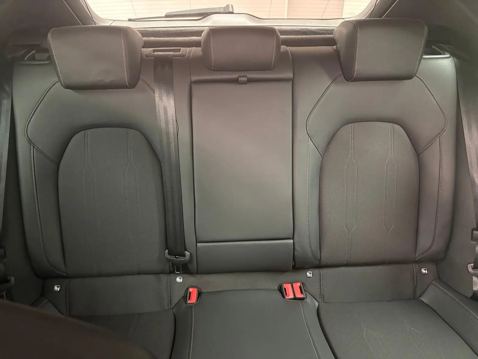 Vue intérieure des sièges arrière en cuir noir avec appuie-têtes et ceinture de sécurité centrale visible.