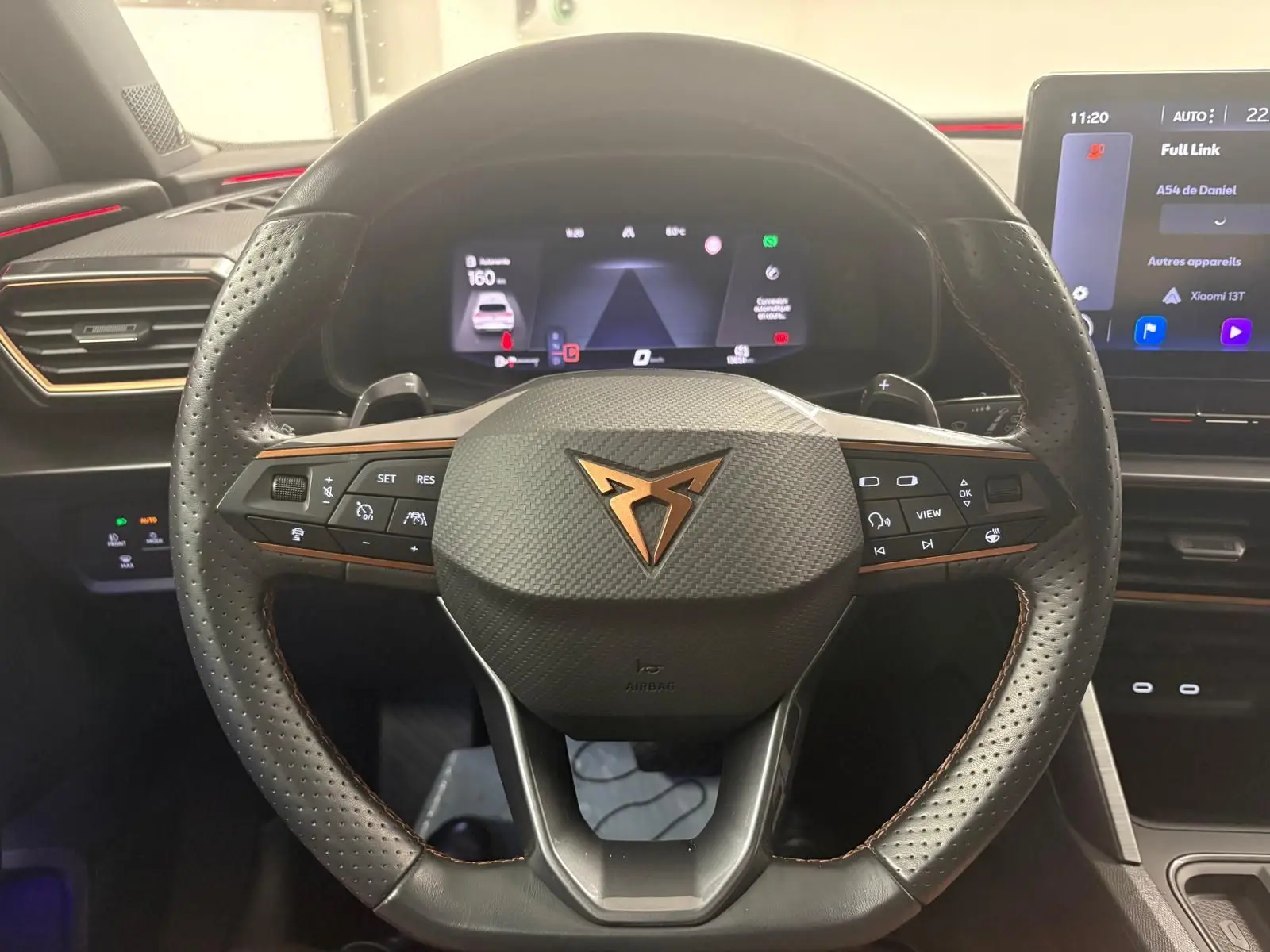 Vue centrée sur le volant perforé noir avec logo CUPRA cuivré, tableau de bord numérique et écran tactile intérieur.