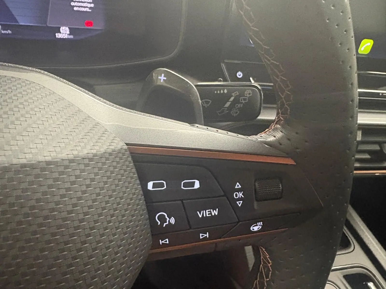 Gros plan sur le volant perforé de la CUPRA Leon blanc Nevada 2024 avec commandes intégrées et palettes au volant.