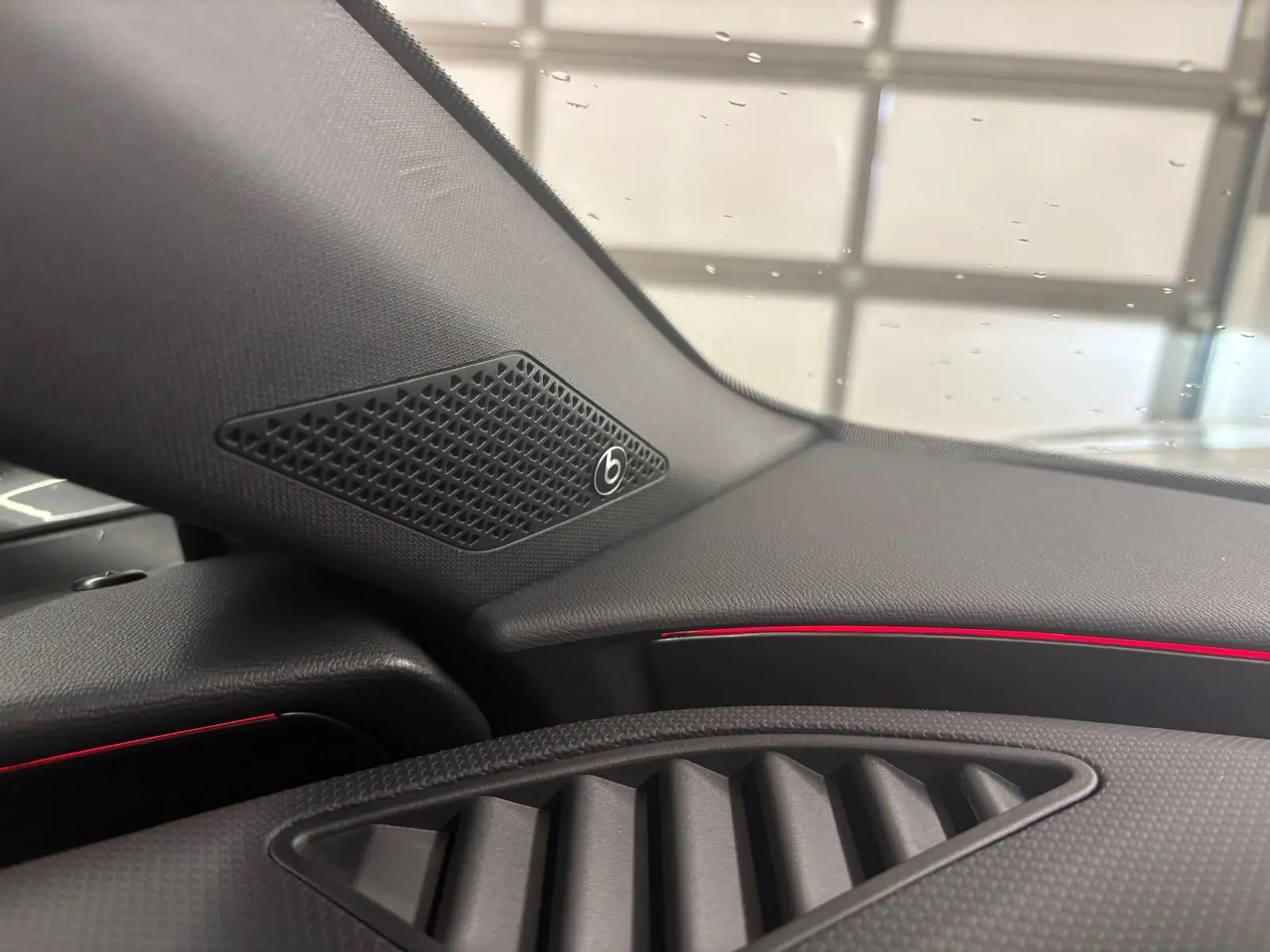 Détail intérieur côté gauche du tableau de bord de la CUPRA Leon 2024 avec haut-parleur Beats et éclairage d'ambiance rouge.