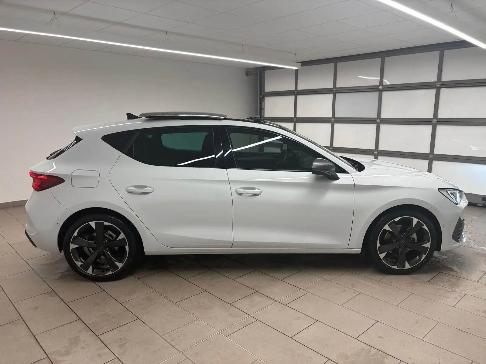 Vue de profil côté gauche d'une CUPRA Leon blanche Nevada avec toit ouvrant panoramique dans un garage.