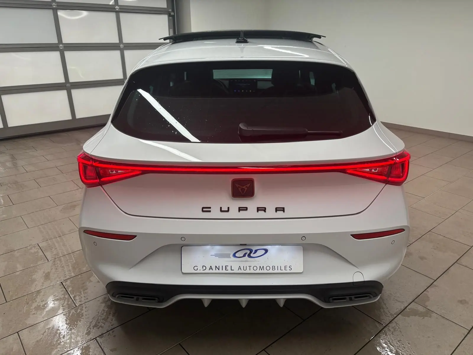 Vue arrière d'une CUPRA Leon blanche Nevada avec feux arrière allumés et toit ouvrant panoramique visible.