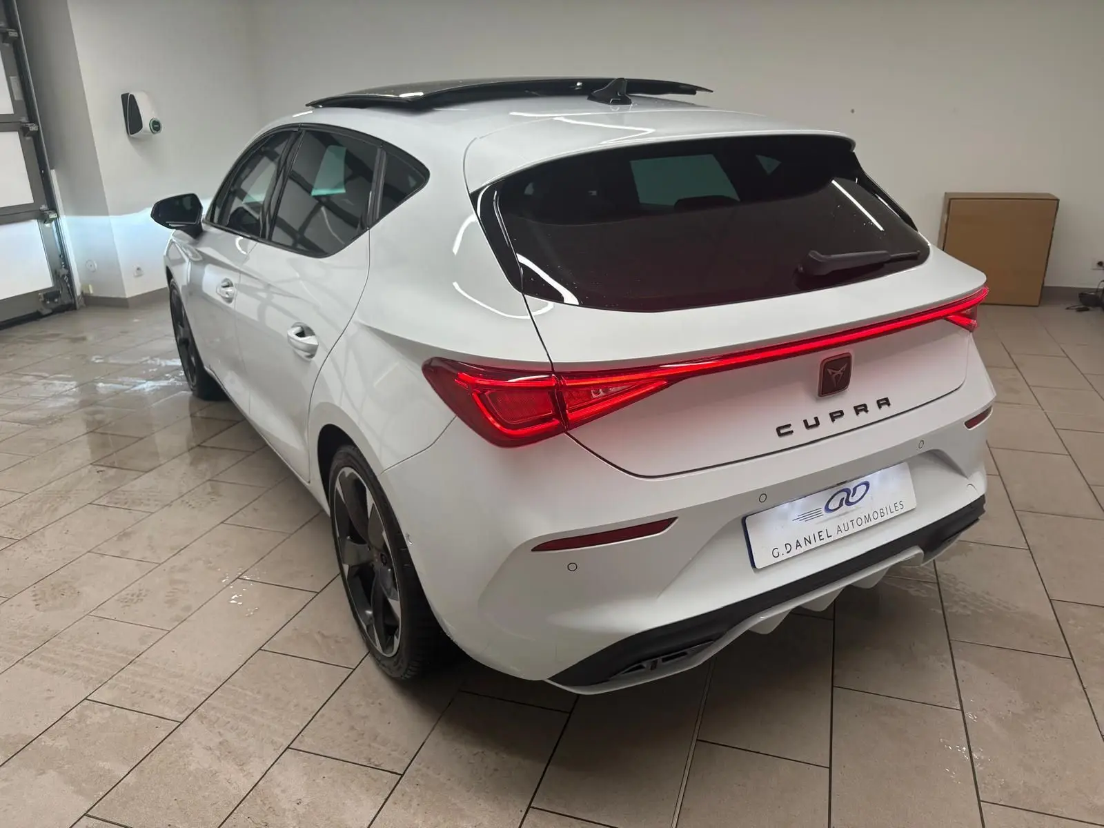 Vue 3/4 arrière droite d'une CUPRA Leon blanche Nevada avec toit ouvrant panoramique et feux arrière allumés.