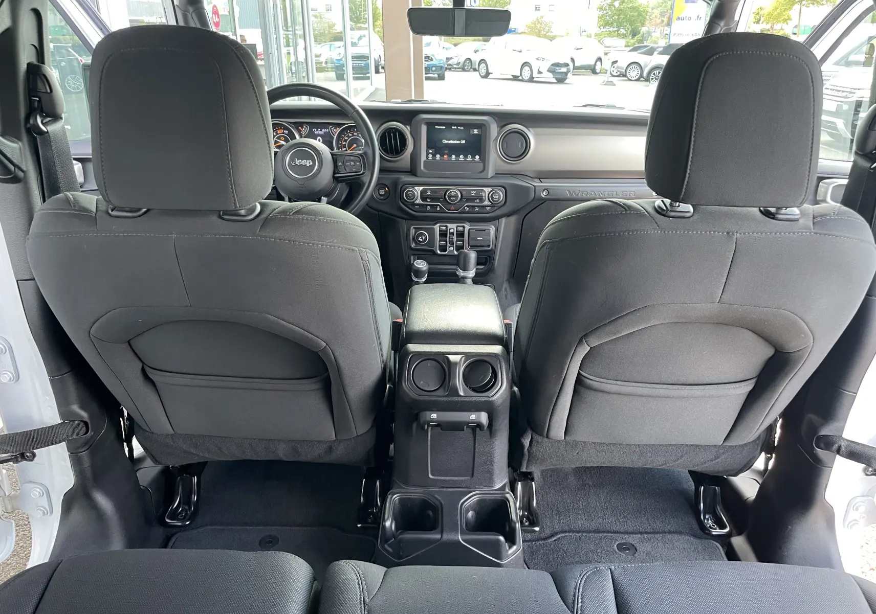 Vue intérieure arrière du Jeep Wrangler blanc 2018, montrant les sièges noirs et le tableau de bord avec écran tactile central.