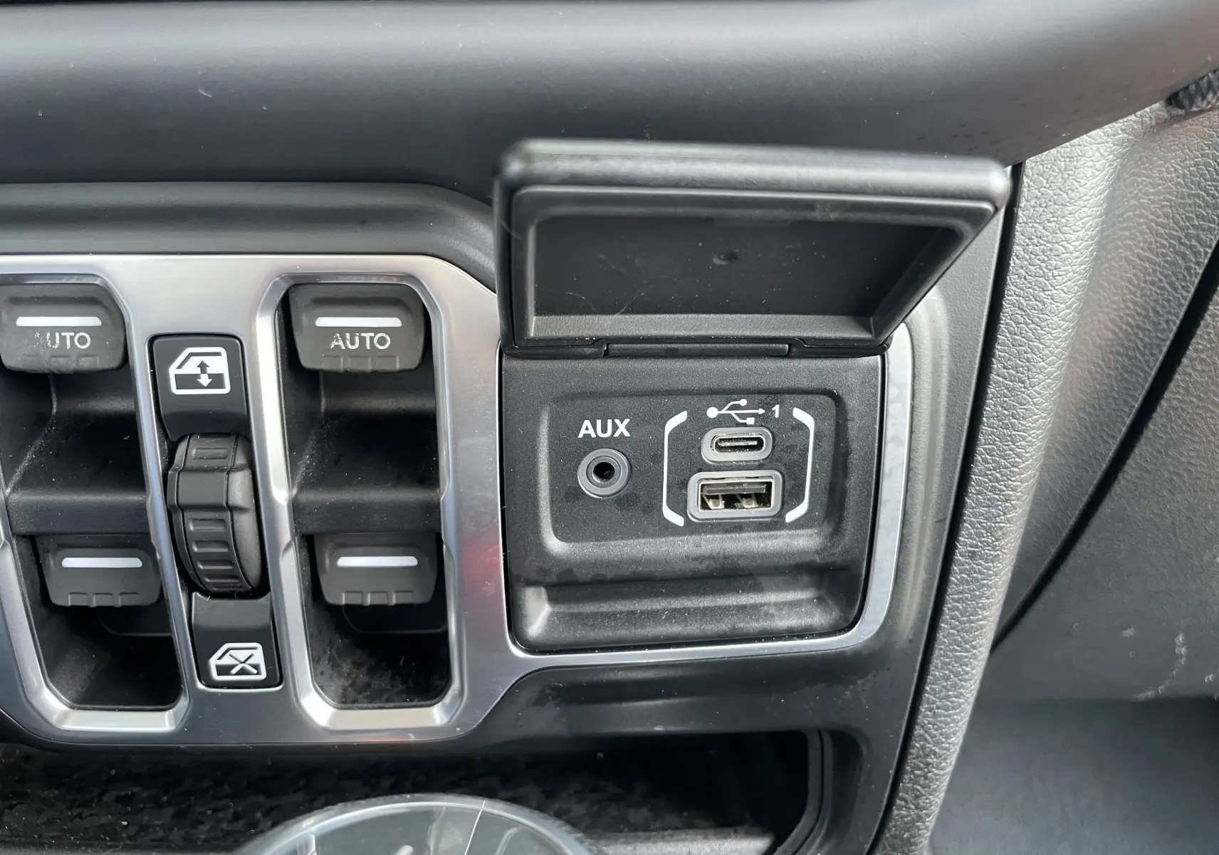 Gros plan sur les commandes des vitres électriques et les ports USB et AUX du tableau de bord d'une Jeep Wrangler blanche de 2018.