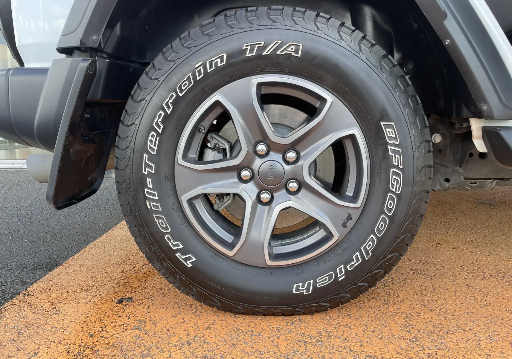 Gros plan sur la roue avant gauche du Jeep Wrangler blanc, mettant en valeur la jante grise et le pneu BFGoodrich Trail-Terrain.