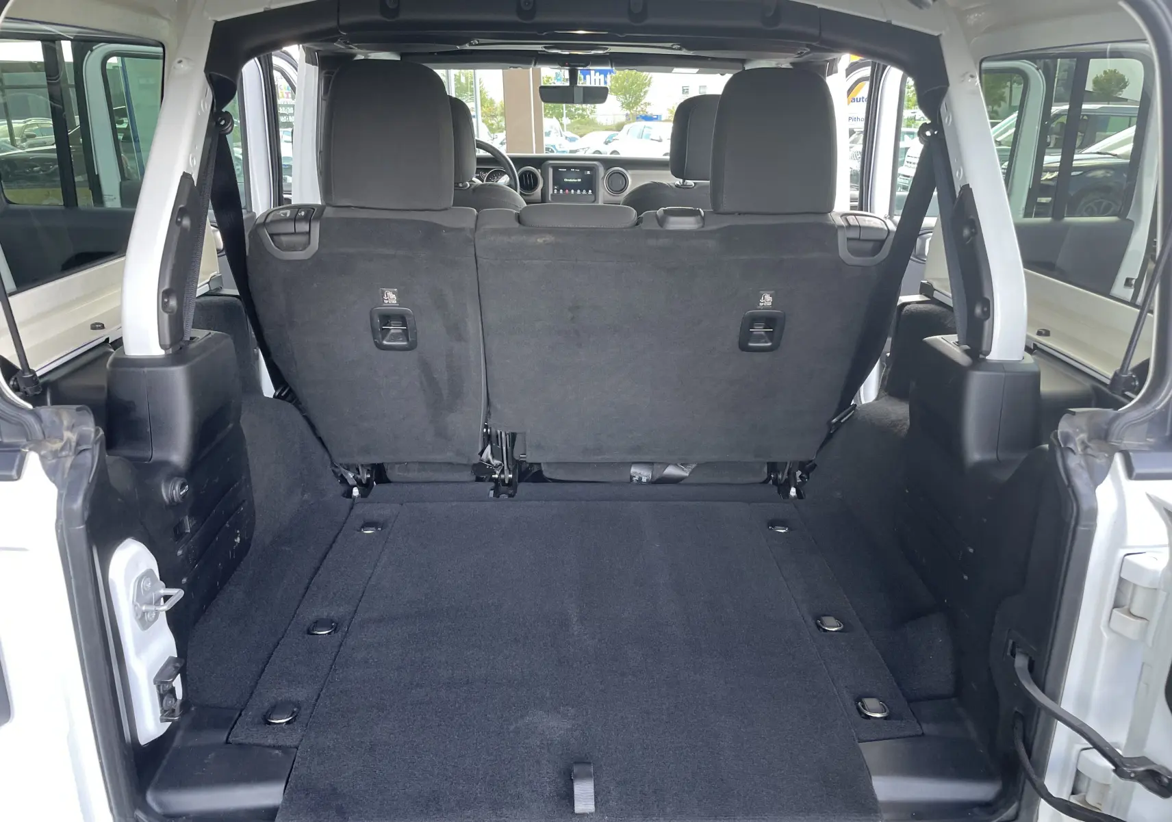 Coffre ouvert du Jeep Wrangler blanc 2018, vue depuis l'arrière montrant banquette arrière et espace de chargement spacieux.