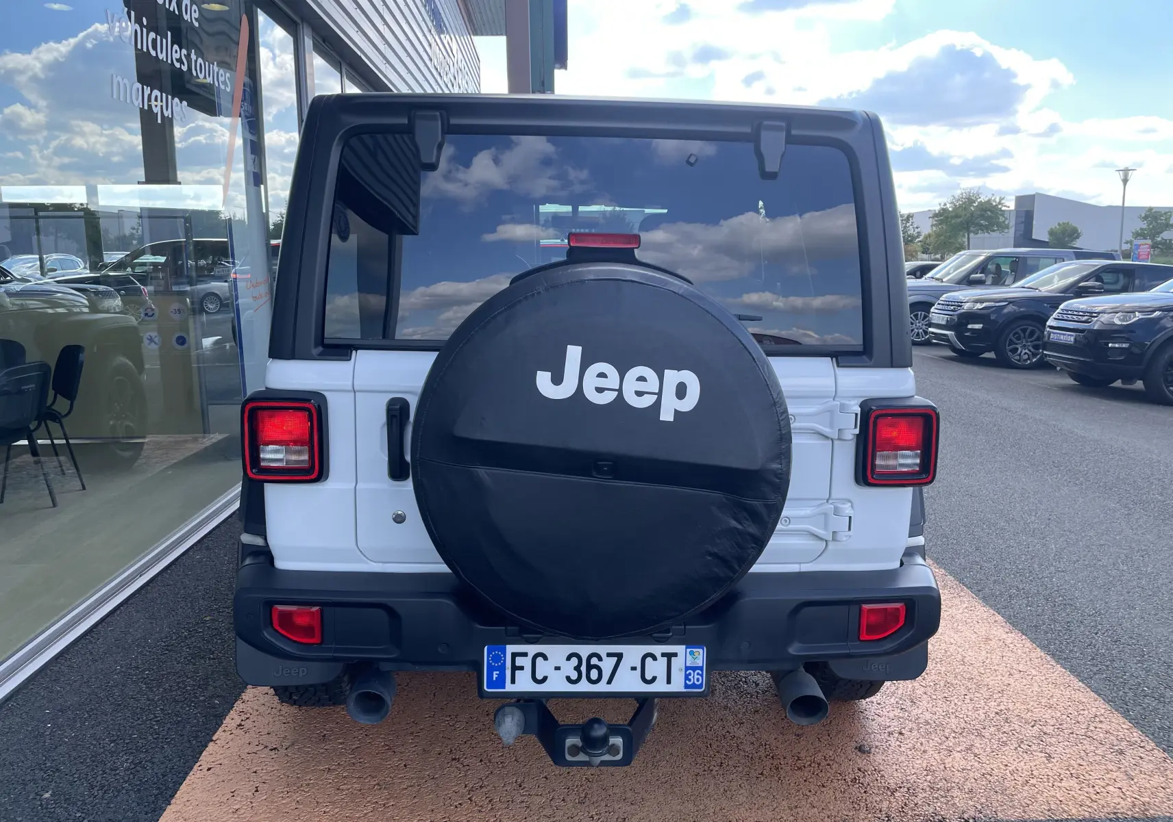 Vue arrière d'un Jeep Wrangler blanc de 2018 avec roue de secours couverte et feux carrés rouges.