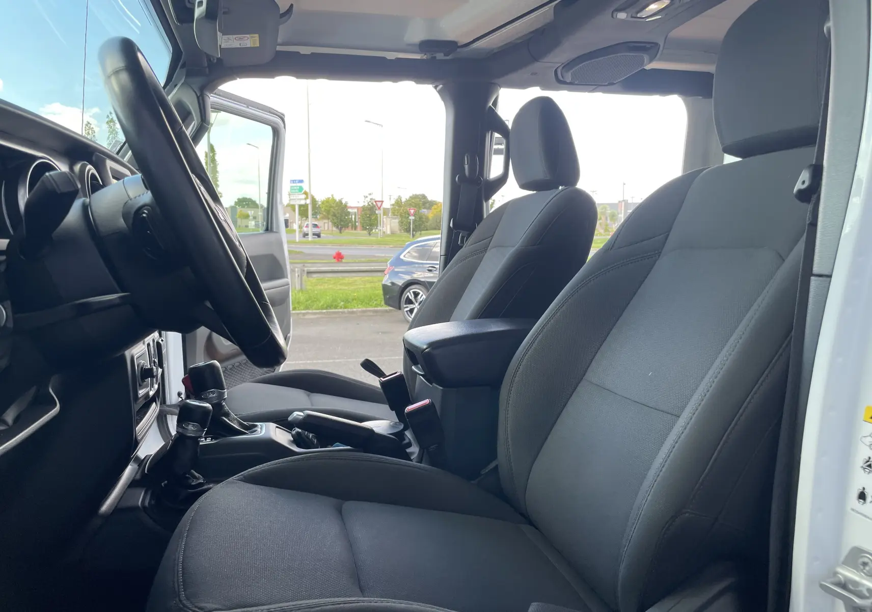 Intérieur avant du Jeep Wrangler blanc 2018, sièges tissu noirs et tableau de bord avec volant visible côté gauche.