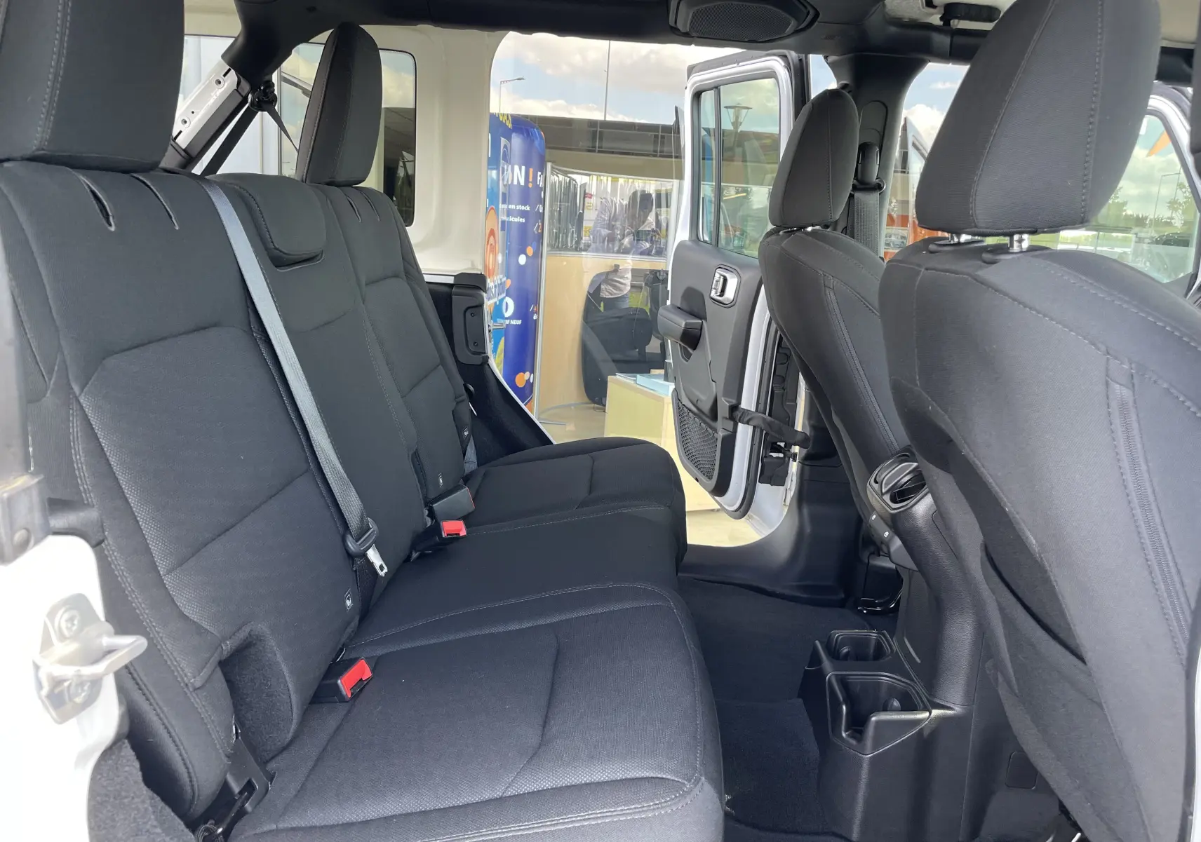 Vue intérieure arrière droite du Jeep Wrangler blanc 2018, sièges tissu noir et portes ouvertes sur l'extérieur.