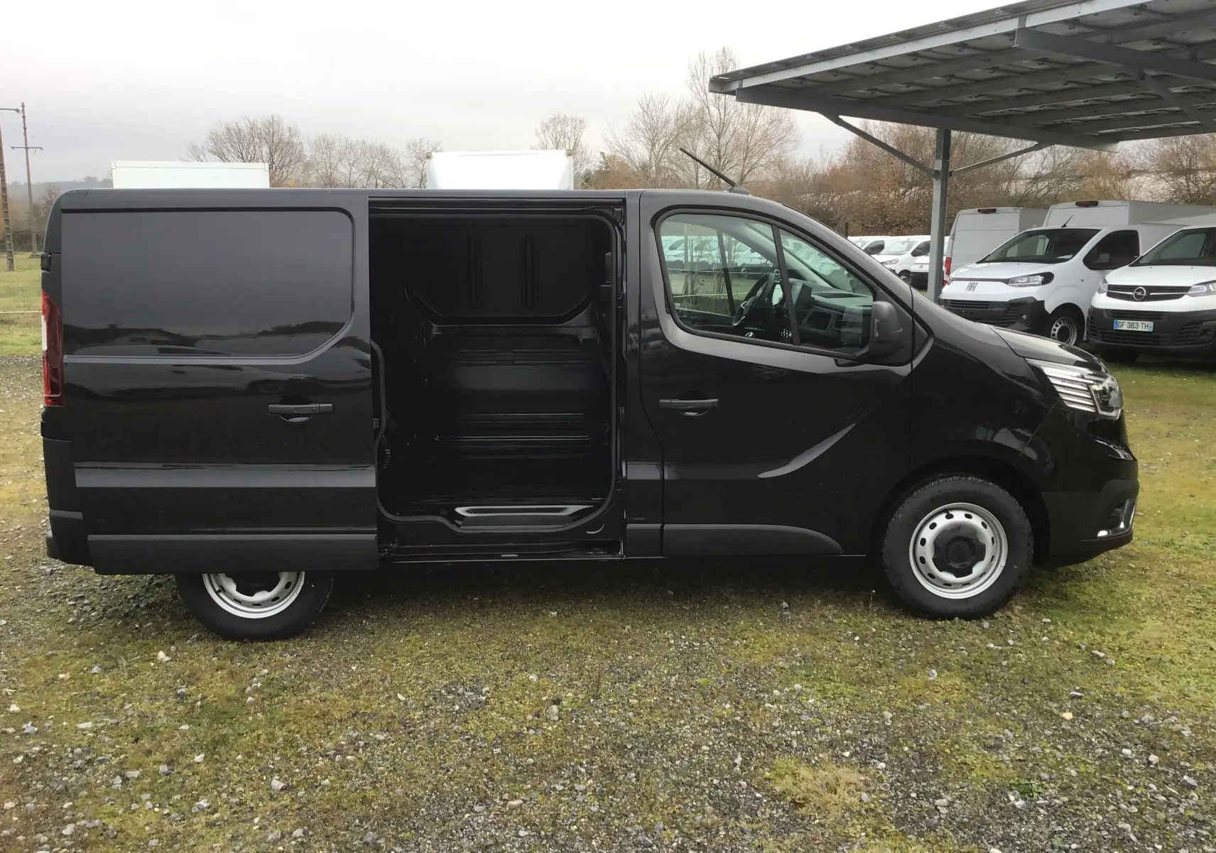 Vue de profil côté gauche d'un Renault Trafic Fourgon noir 2025 avec porte coulissante ouverte révélant l'espace de chargement.