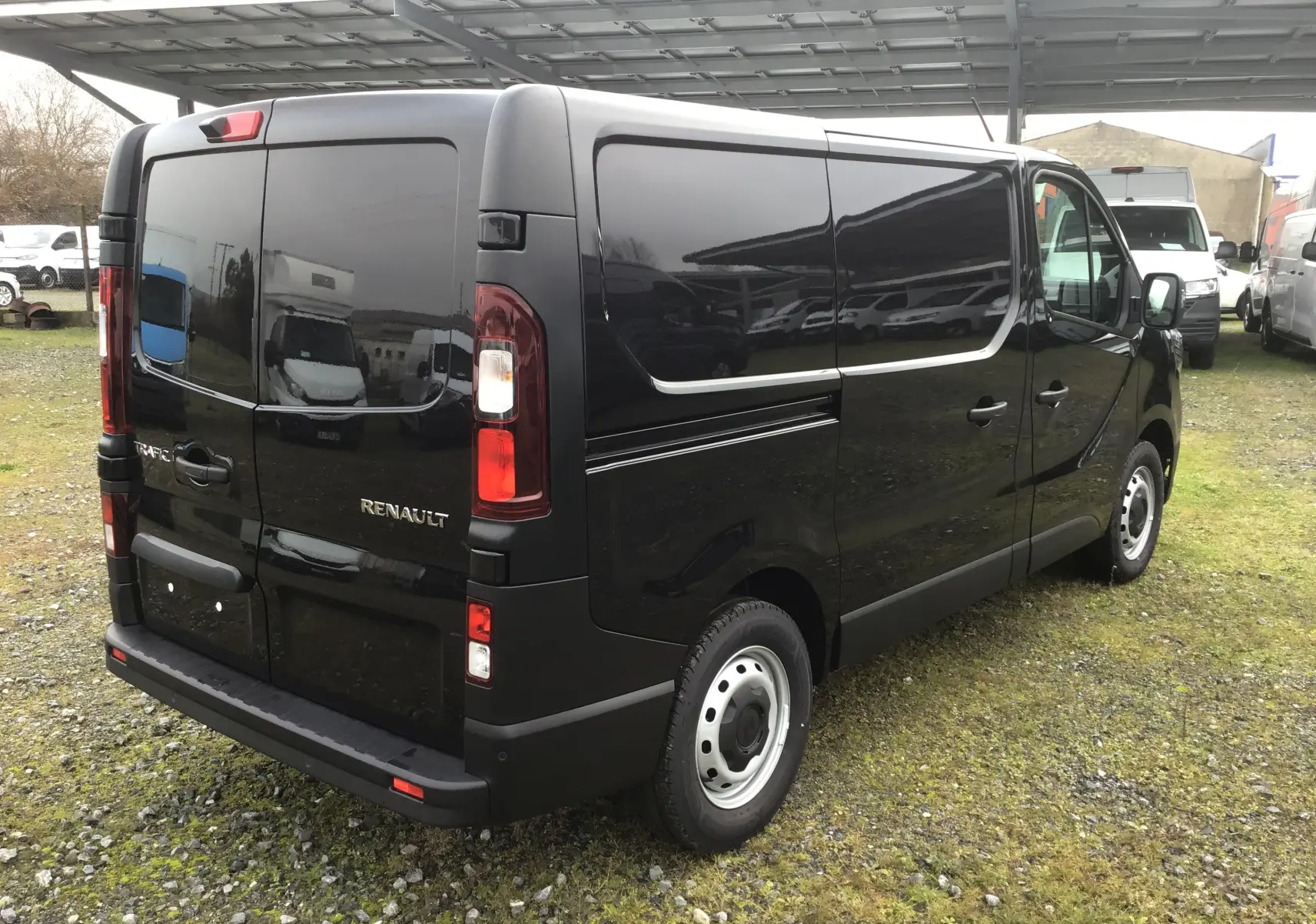 Vue 3/4 arrière droite du Renault Trafic Fourgon noir, mettant en valeur ses portes arrière battantes et ses feux verticaux.