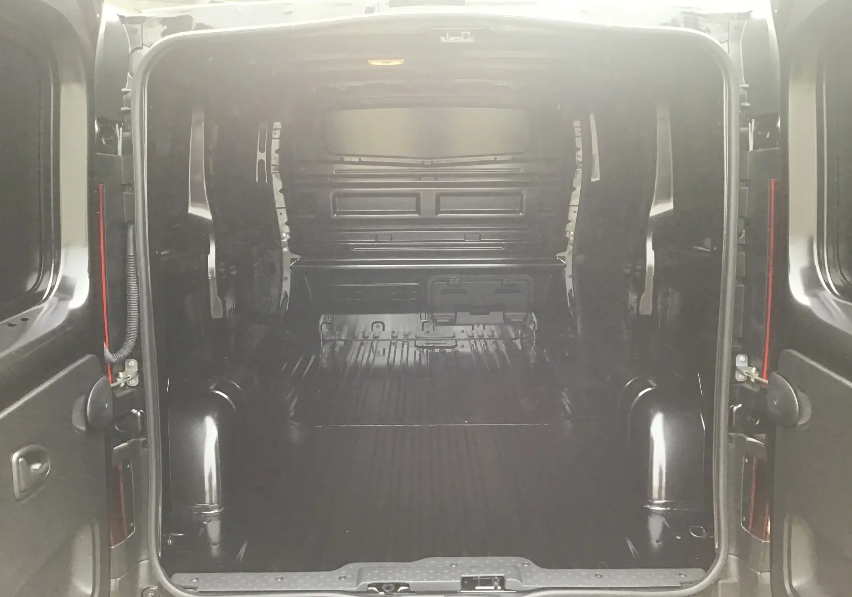 Vue arrière du fourgon Renault Trafic L1H1 noir, montrant l’espace de chargement vide et les portes ouvertes.