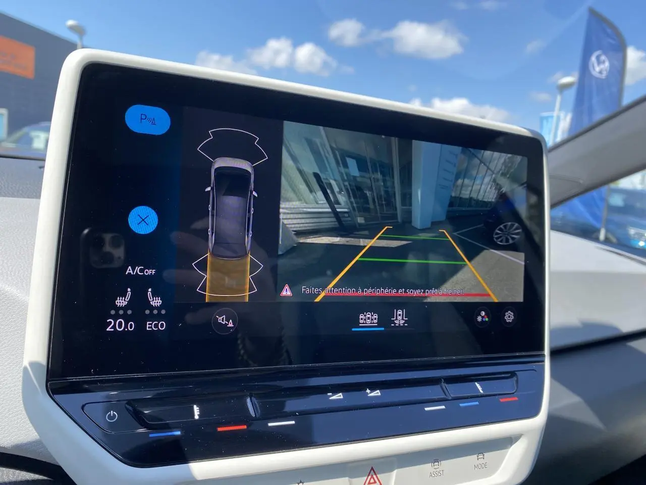 Écran central du Volkswagen ID.3 blanc montrant la caméra de recul et l'aide au stationnement en extérieur.