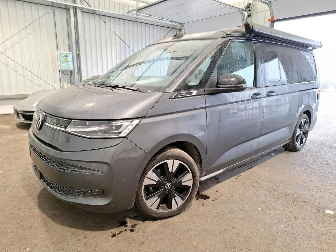 Vue 3/4 avant droit du Volkswagen California T7 2.0 TDI 150 DSG Ocean gris Indium avec jantes alliage noires brillantes.