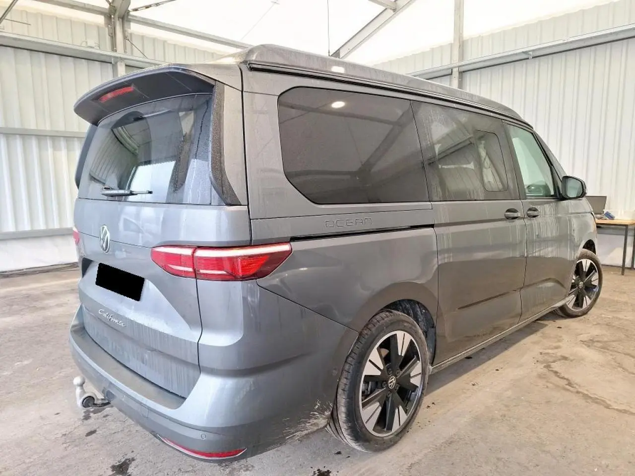 Vue 3/4 arrière droite du Volkswagen California T7 2.0 TDI gris Indium avec jantes alliage noir brillant et attelage rabattable.