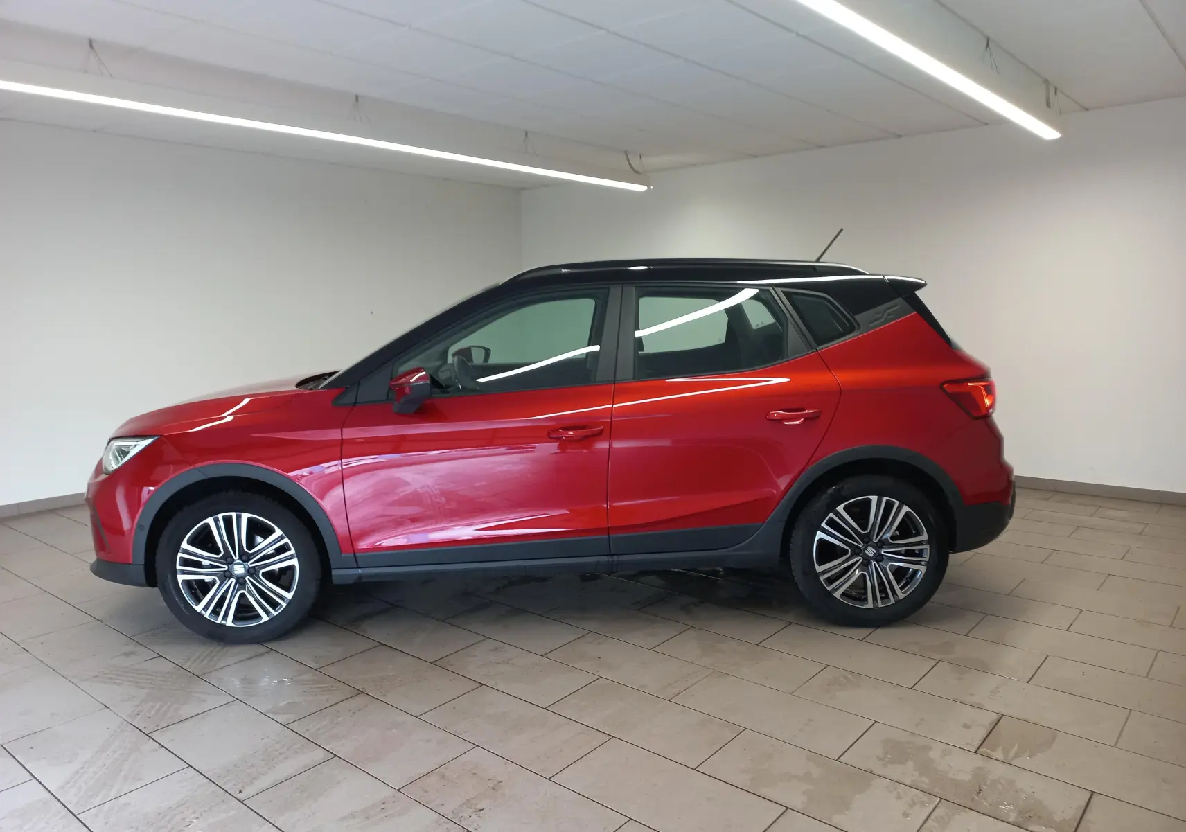 Vue de profil côté gauche d'un SEAT Arona 2025 rouge Désir avec toit noir Minuit et jantes alliage.