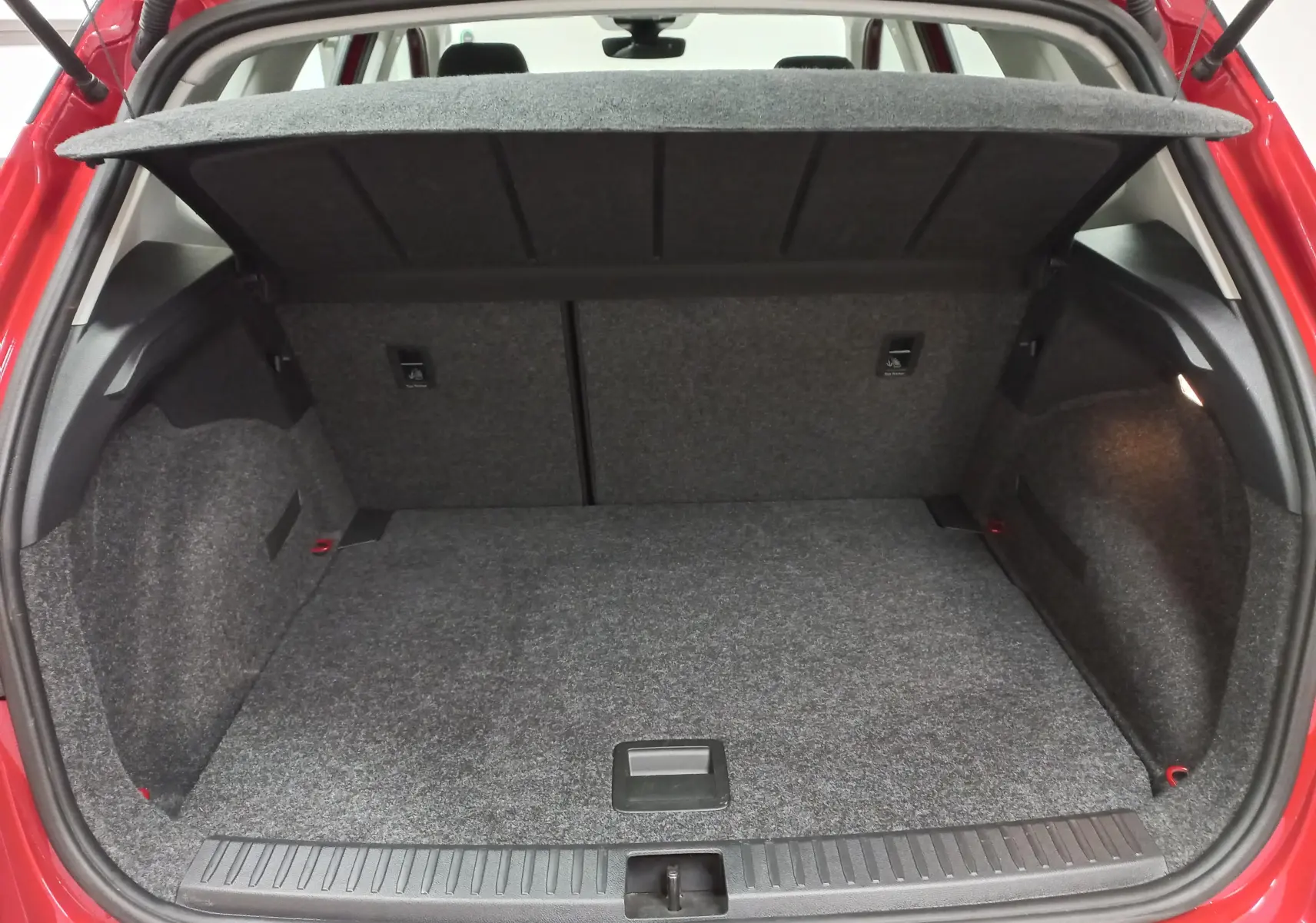 Coffre ouvert vu de l’arrière d’un SEAT Arona rouge Désir avec toit noir, montrant l’espace de chargement vide et la moquette grise.