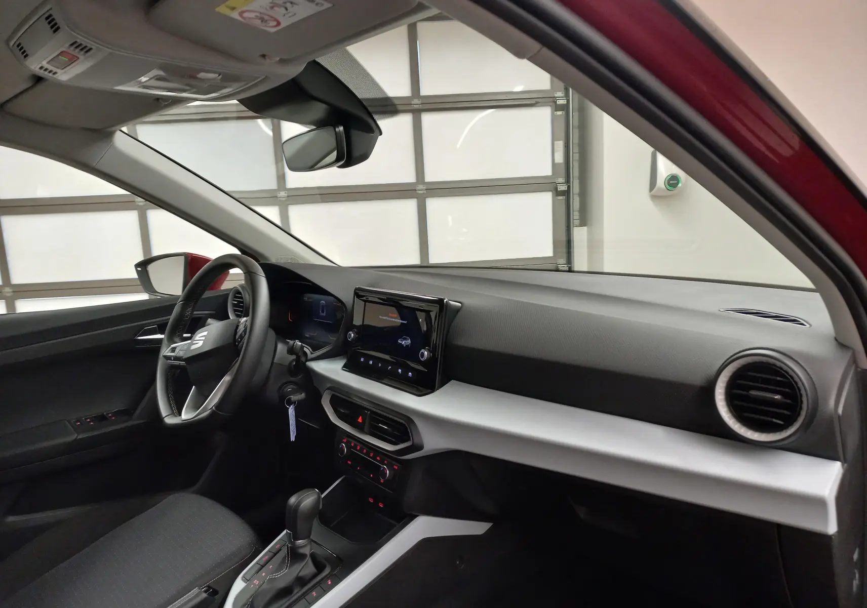 Vue intérieure côté conducteur du SEAT Arona rouge Désir avec tableau de bord moderne et écran tactile central.
