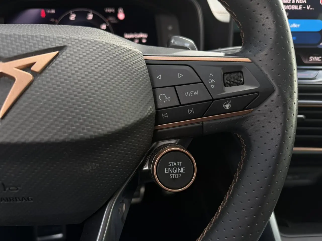 Détail du volant perforé noir avec logo CUPRA cuivre et bouton start/stop sur la droite, intérieur moderne.