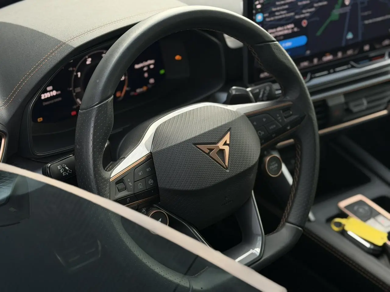 Gros plan sur le volant cuir noir perforé avec logo CUPRA cuivré, tableau de bord digital et console centrale du Formentor blanc.