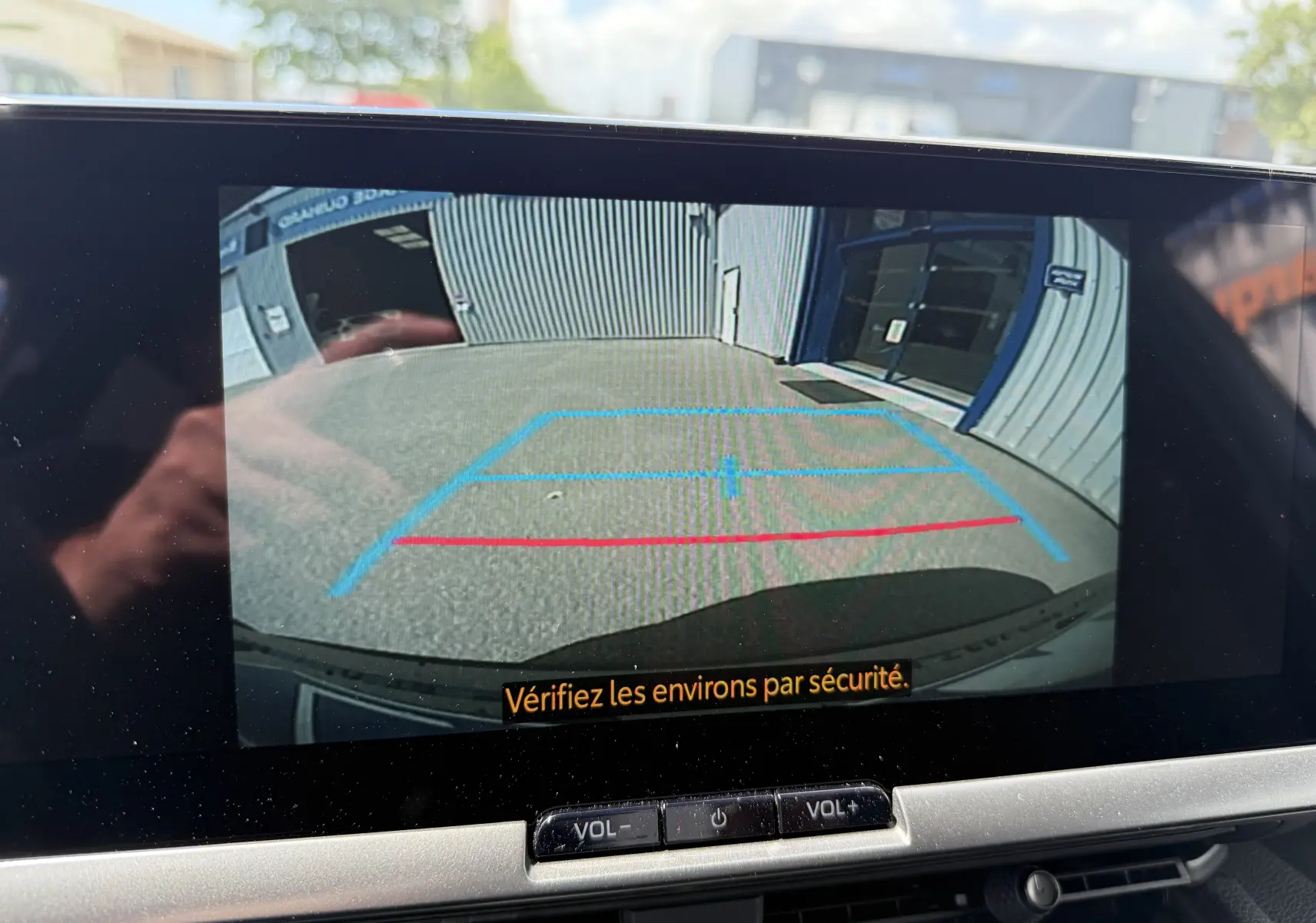 Vue caméra de recul du Toyota C-HR 1.8 Hybride gris atlas montrant les lignes de guidage sur un sol extérieur devant un bâtiment.