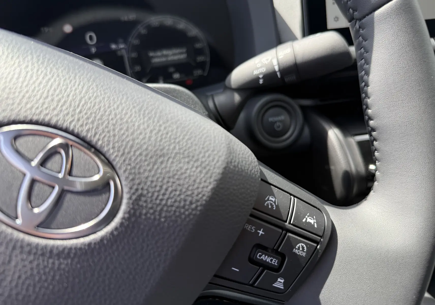 Gros plan sur le volant gris du Toyota C-HR 1.8 Hybride 2025, avec commandes d’aide à la conduite visibles.