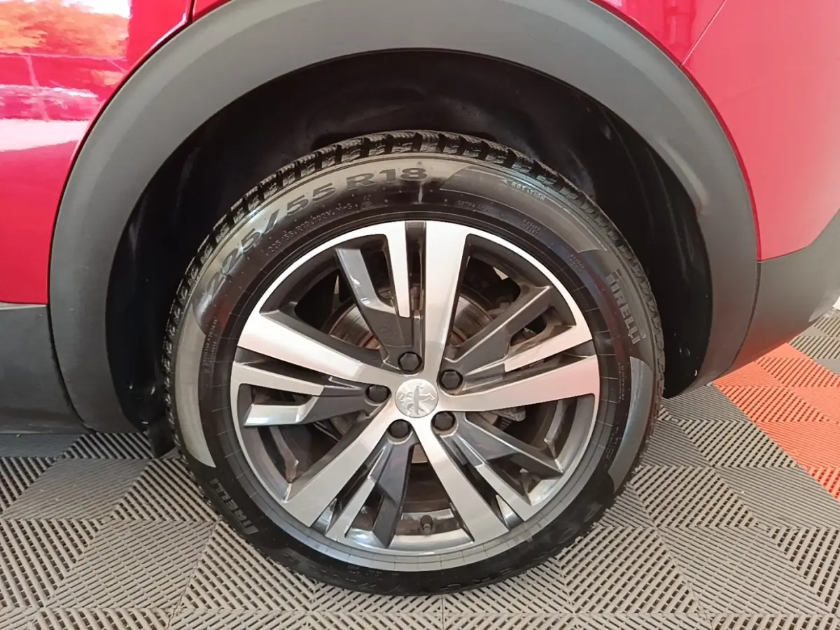 Gros plan sur la roue avant droite du Peugeot 3008 rouge, mettant en valeur la jante alliage bicolore et le pneu Pirelli.
