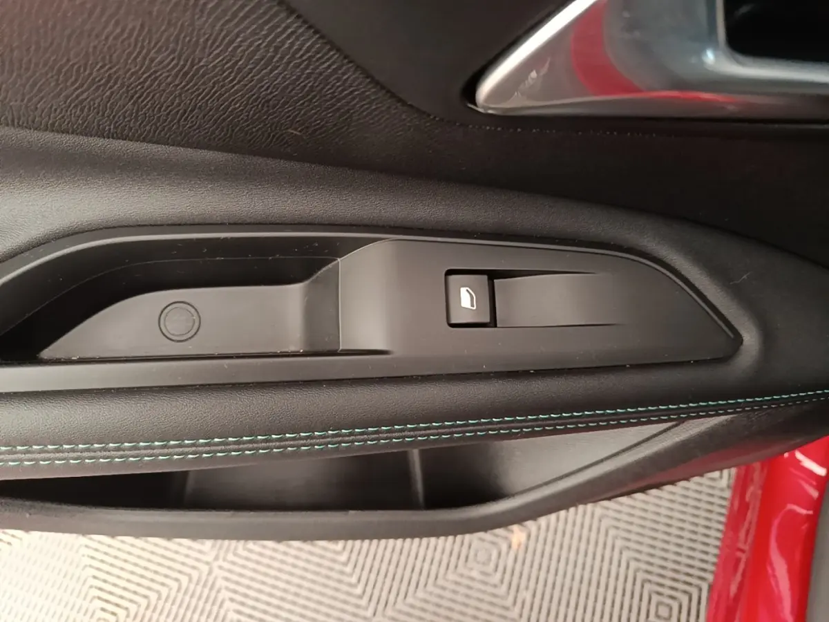 Détail de la poignée intérieure côté conducteur du Peugeot 3008 rouge avec couture bleue sur la garniture de porte noire.