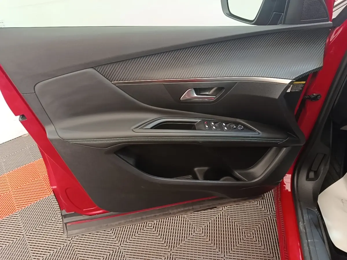 Vue intérieure côté gauche de la porte avant rouge du Peugeot 3008 avec garniture noire et commandes électriques.