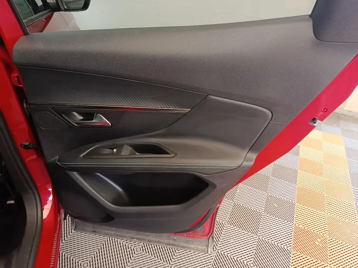 Vue rapprochée de la porte avant gauche rouge du Peugeot 3008, avec garniture noire et poignée métallique.