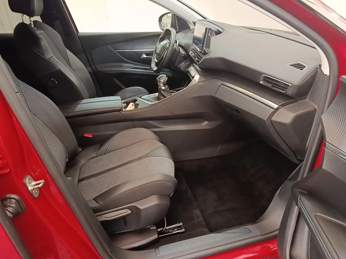 Vue intérieure côté passager avant d’un Peugeot 3008 rouge, sièges tissu et cuir noir, tableau de bord moderne avec écran tactile.