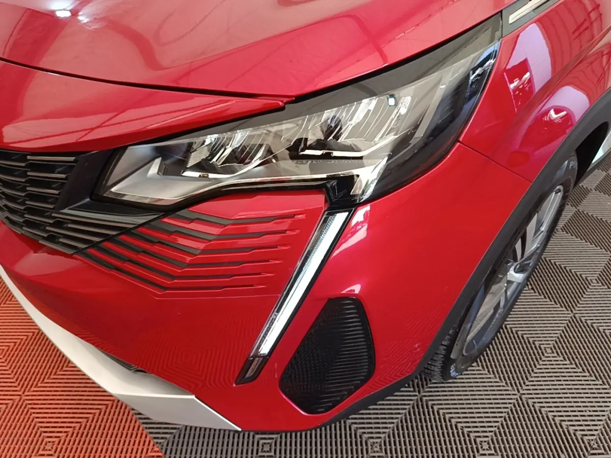 Gros plan sur l’avant droit rouge vif du Peugeot 3008, mettant en valeur le phare LED et la calandre noire.