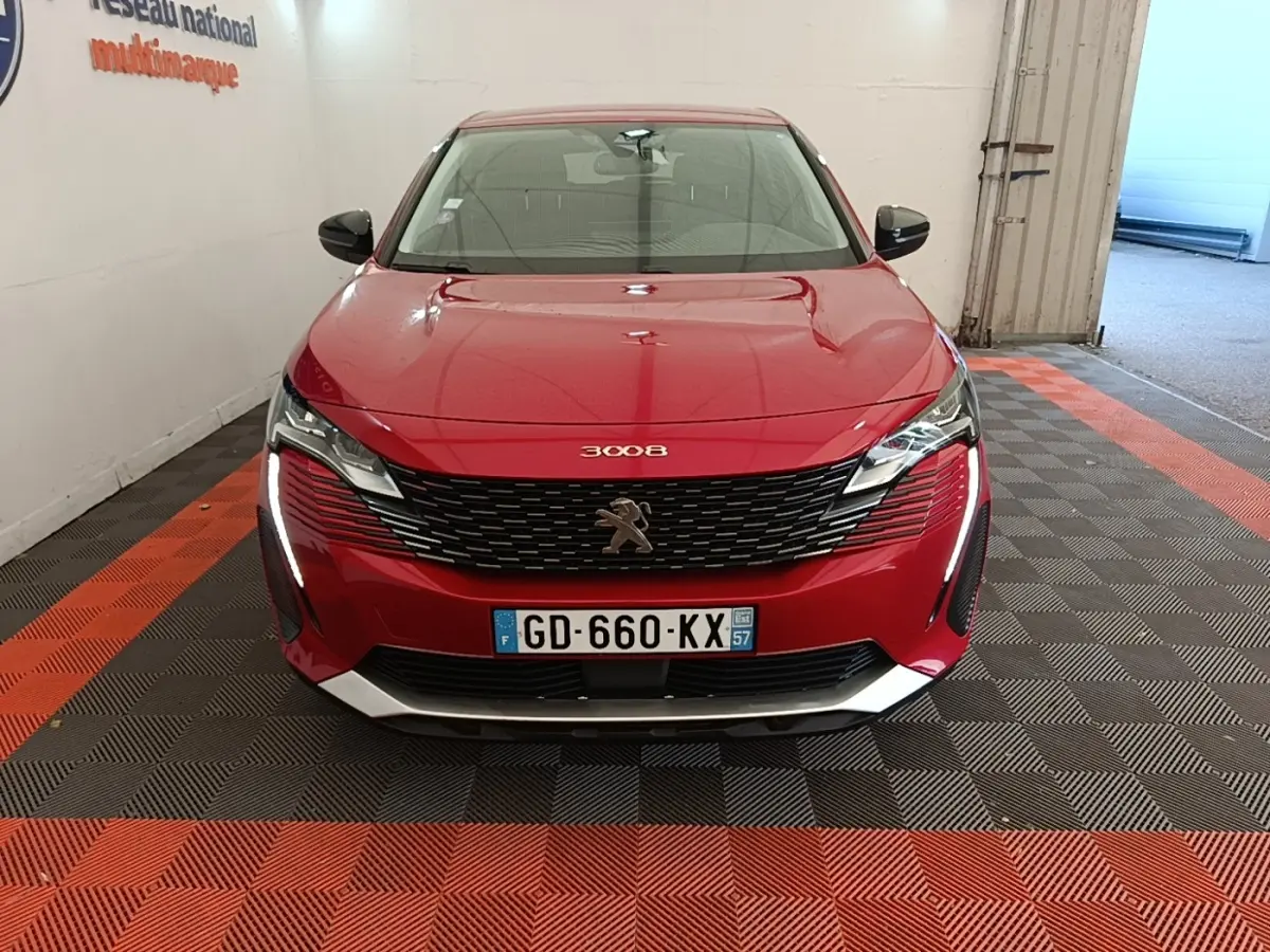 Vue avant frontale d'un Peugeot 3008 rouge avec calandre noire et feux LED verticaux allumés dans un garage.