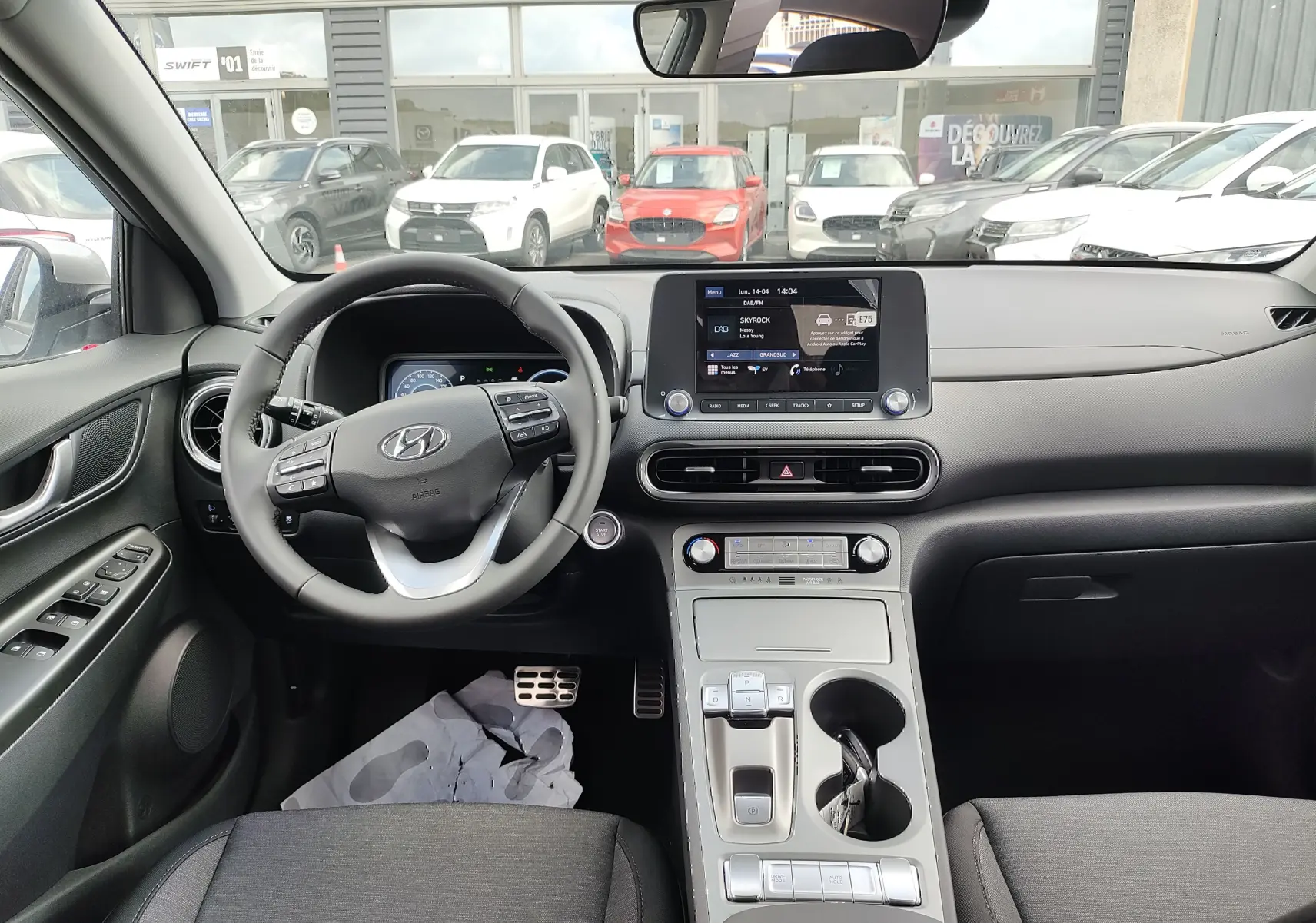 Vue intérieure du tableau de bord et volant cuir noir du Hyundai Kona Electric 2025, avec écran tactile central et commandes au volant.