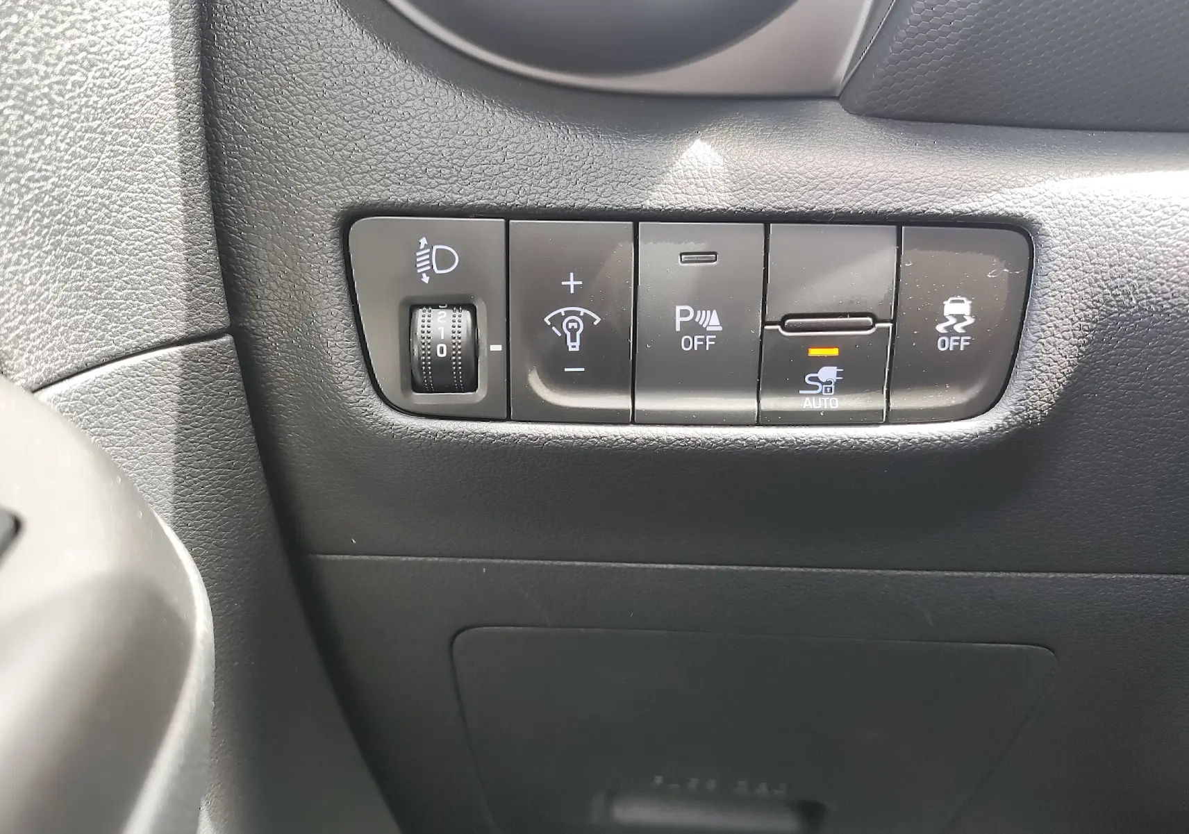 Vue rapprochée des commandes de réglage des phares et aides à la conduite sur le tableau de bord noir du Hyundai Kona électrique gris.