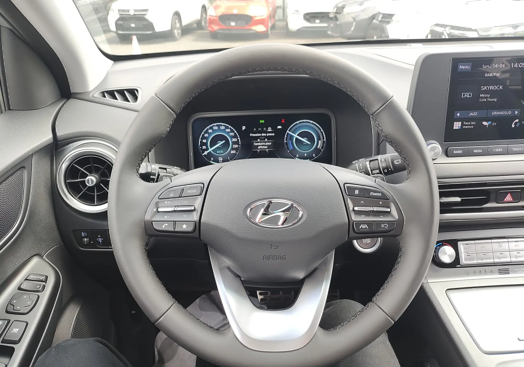 Vue intérieure centrée sur le volant cuir et tableau de bord numérique du Hyundai Kona Electric gris métallisé 2025.