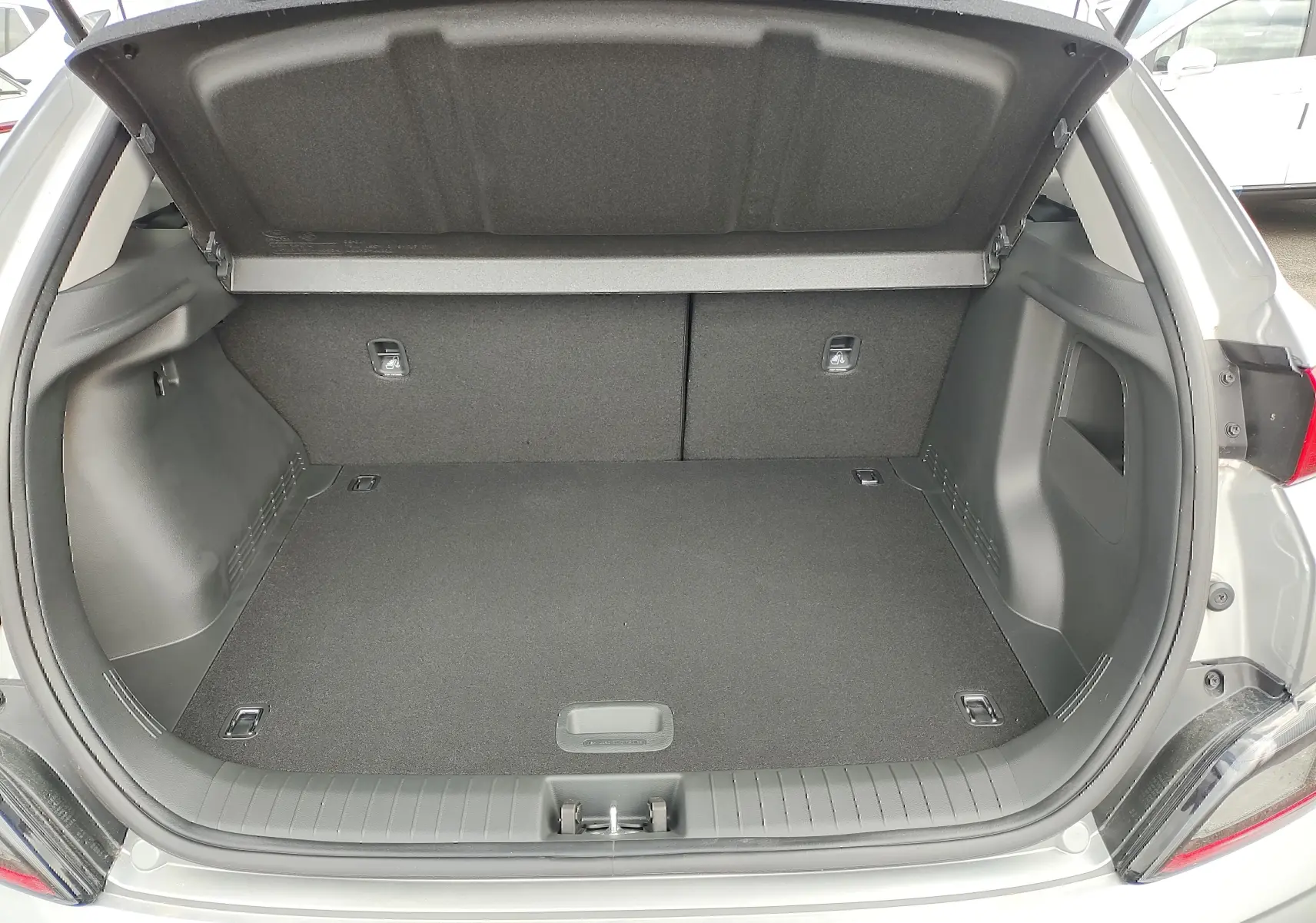 Coffre ouvert vu de l'arrière d'un Hyundai Kona Electric gris métallisé, espace de chargement vide et propre.