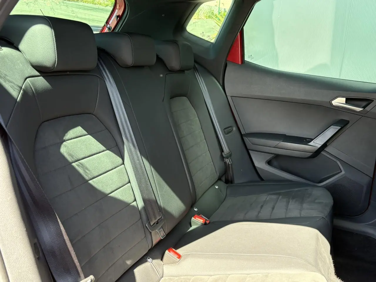 Vue latérale droite de la banquette arrière noire en suédine du SEAT Arona Rouge Désir avec ceinture et porte intérieur visible.